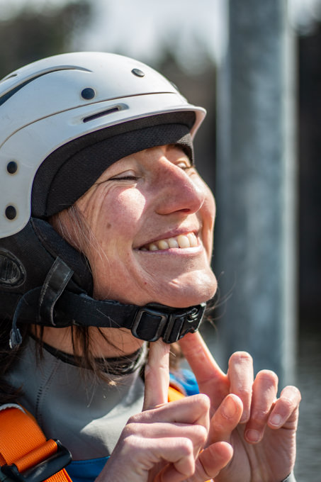 A woman tries to slide the chin strap of her helmet forward over her chin.