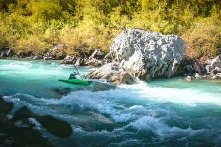 Ein Kajakfahrer in einem grünen Kajak fährt eine kleine Stufe bei einem F1 Kurs auf einem türkisen Fluss